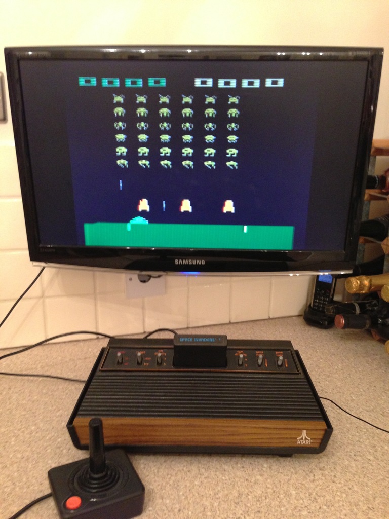 Woodgrain Atari 2600 with joystick, playing Space Invaders on a Samsung TV